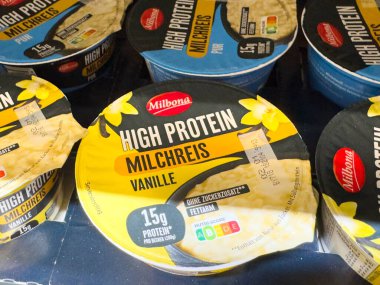 Villach, Avusturya - 02 Aralık 2025: Vanilya aromalı Milbona yüksek proteinli sütlaç bardakları, besin faydalarını ve çekici ambalajları vurgulayarak raflarda güzelce düzenlenmiştir