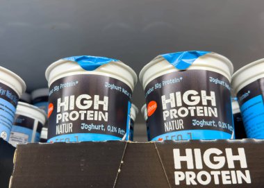 Villach, Avusturya - 02 Aralık 2025: Yüksek proteinli yoğurt bardakları, sağlıklı seçenekler arayan tüketiciler için markalaşma ve beslenme detaylarını ön plana çıkaran süpermarket raflarında düzenlenmiştir