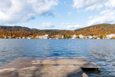 Güz ormanı ve bulutlu gökyüzü ile sakin göl manzarası.