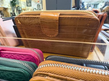Villach, Avusturya - 10 Aralık 2025: Kahverengi timsah derisi cüzdan, çağdaş moda eğilimlerini ve dokularını vurgulayarak, bir butikte canlı cüzdanlar arasında yer alır.