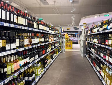 Villach, Avusturya - 10 Aralık 2025: Modern süpermarket şarap reyonu, alışveriş deneyimini geliştiren parlak ışıklarla aydınlatılmış raflarda çeşitli şişe çeşitliliğine sahiptir.