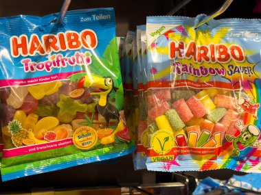 Villach, Avusturya - 10 Aralık 2025: Tropifrutti ve Gökkuşağı Koruyucusu da dahil olmak üzere HARIBO şeker paketleri, renkli jelibon şekerleri ve eğlenceli tasarımları ön plana çıkaran bir rafta düzenlenmiştir.