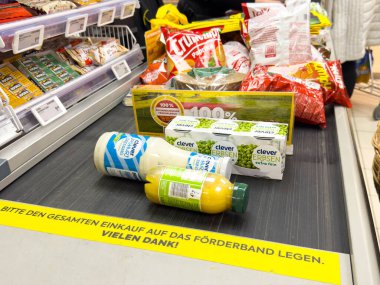 Villach, Avusturya - 10 Aralık 2025: Bakkal ürünleri arasında kasadaki taşıma bandındaki içecekler ve atıştırmalıklar, alışveriş atmosferi ve renkli ambalajlar yer alıyor