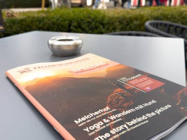 Velden, Avusturya - 06 Aralık 2025: Mum tutacağıyla bir masada seyahat dergisi, açık hava maceraları ve ilham verici keşif hikayeleri