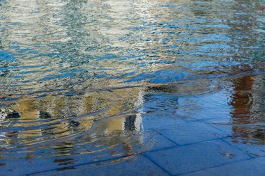 Dalgalanma desenleri ve renkli yansımaları olan yansıtıcı su yüzeyi.