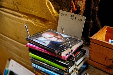 Venedik, İtalya - 05 Aralık 2025: Tahta kutu ve fiyat etiketli kırsal bir ortamda bir adamın portresi ile bir film kapağı sergilenen DVD yığını