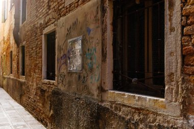 Venedik, İtalya - 05 Aralık 2025: Venedik 'teki dar bir sokakta, tarihi mimarinin ortasındaki kentsel sanatı vurgulayan, canlı graffitilerle dolu, rustik tuğla duvarlar bulunuyor