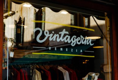 Venedik, İtalya - 05 Aralık 2025: Venedik 'teki vintage mağazasının vitrininde çeşitli renkli kıyafetler ve eşsiz moda ürünleri yer alıyor.