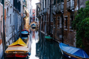 Venedik, İtalya - 05 Aralık 2025: Renkli tekneler, tarihi binalar ve sakin su yansımalarıyla çevrili dar bir Venedik kanalında dizilmiştir.