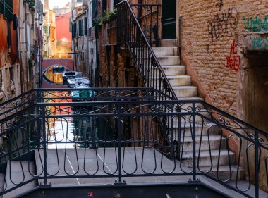 Venedik, İtalya - 05 Aralık 2025: Venedik 'te dar kanallarda sakin sulara yansıyan dekoratif bir köprü ve renkli binalar sergileniyor