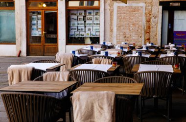 Venedik, İtalya - 05 Aralık 2025: Ahşap masaları ve sandalyeleri olan boş bir kafeterya, koltuklarda rahat battaniyeler, yemek için davetkar bir ortam yaratmak