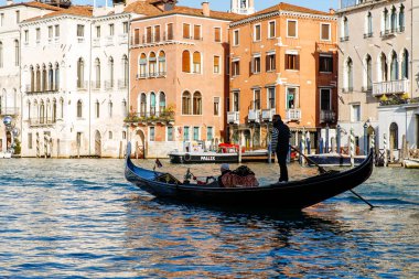 Venedik, İtalya - 05 Aralık 2025 Gondolcu, Venedik 'in kanalı boyunca süzülerek renkli binalar ve ışıldayan suyla çevrili bir gondolda duruyor.