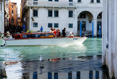 Venedik, İtalya - 5 Aralık 2025: Turistler Venedik 'in fevkalade kanallarında, büyüleyici mimari ve parıltılı yansımalarla çevrili bir tekne turunun tadını çıkarıyorlar.