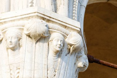 Venedik, İtalya - 05 Aralık 2025: İnsan yüzleri ve çiçek desenlerinin detaylı oymalarının yer aldığı tarihi sütun, taş mimarideki sanat ve zanaatkarlığı vurguluyor