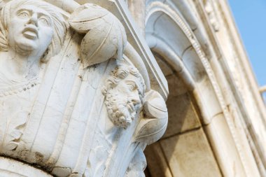 Venedik, İtalya - 05 Aralık 2025: Süslü taş sütun, insan yüzleri ve yapraklarının ayrıntılı oymalarını sergiliyor, tarihsel ortamdaki klasik mimariyi vurguluyor