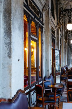 Venedik, İtalya - 05 Aralık 2025: Konforlu kafe içi klasik ahşap sandalyeler ve masalar, sıcak ışıklandırma ve tarihi mimari konukları dinlenmeye ve eğlenmeye davet ediyor