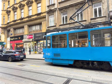 Zagreb, Hırvatistan - 14 Aralık 2025: Mavi tramvay, dükkanlar ve arabalarla hareketli caddelerde hareket ederek kentsel ulaşım ve günlük yaşamın özünü yakalıyor