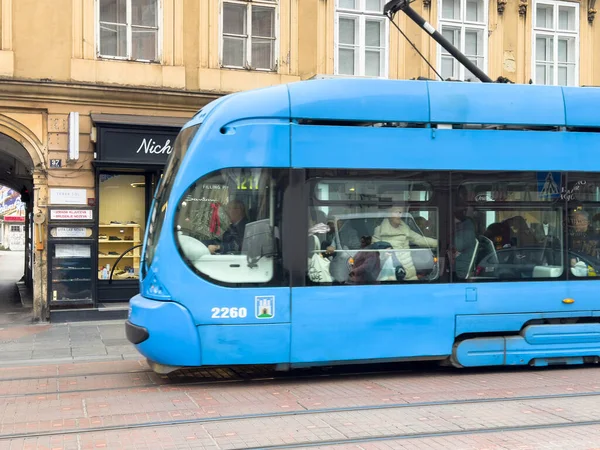 Zagreb, Hırvatistan - 14 Aralık 2025: Butik dükkanı yakınlarındaki şehir caddesi boyunca mavi tramvay seferi, hareketli bir ortamda kentsel yaşam ve toplu taşımacılığı vurguluyor