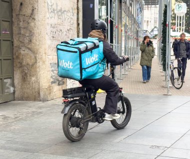 Zagreb, Hırvatistan - 14 Aralık 2025: Kent caddesinde gezinen elektrikli bisiklete binen Wolt kuryesi, yayalarla kentsel gıda dağıtım deneyimini ön plana çıkardı