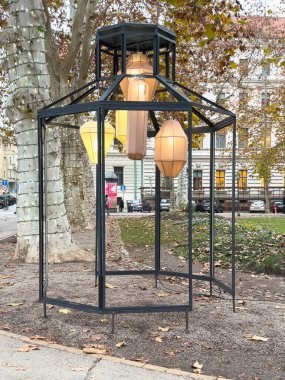 Zagreb, Hırvatistan - 14 Aralık 2025: Açık hava lambası kurulumunda, halka açık bir park ortamında ağaçlarla çevrili sanatsal tasarım ve sıcak ışıklandırma yer alıyor