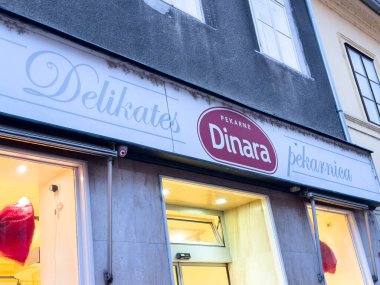 Zagreb, Hırvatistan - 14 Aralık 2025: Alacakaranlıkta Dinara fırınının dış tarafında, aydınlık tabelalar ve cazip hamur işleri sergilenerek ziyaretçiler için hoş bir ortam yaratıldı