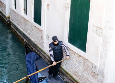 Venedik, İtalya - 19 Şubat 2025: Gondolcu klasik giysiler içinde Venedik 'in pitoresk kanalları boyunca bir gondolda geziniyor, şehrin cazibesini ve tarihini vurguluyor.