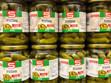 Zagreb, Hırvatistan - 17 Aralık 2025: Bütçe Krastavac turşuları süpermarket raflarında sergilenirken, cam kavanozlarda etiketli parlak yeşil salatalıklar yer alıyor