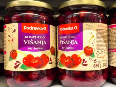Zagreb, Hırvatistan - 17 Aralık 2025: Podravka vişneli komposto kavanozları, şurup ve çekici etiketlerde parlak kırmızı kirazların yer aldığı bir süpermarket rafında düzenlendi