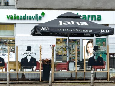 Zagreb, Hırvatistan - 14 Aralık 2025: Jana şemsiyesi, kentsel bir ortamda şık siluetler ve modern markaların yer aldığı eczane girişinde gölge sağlıyor