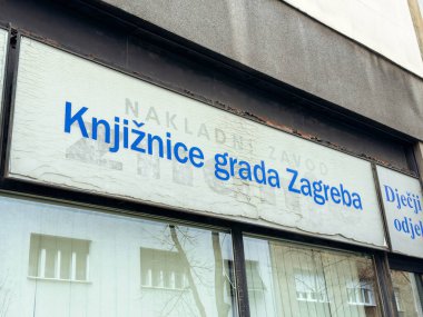 Zagreb, Hırvatistan - 14 Aralık 2025: Yıpranmış bir cephede, yerel kültür ve toplumla bağlantıyı temsil eden mavi harfli kentsel alanda halk kütüphanesi işareti