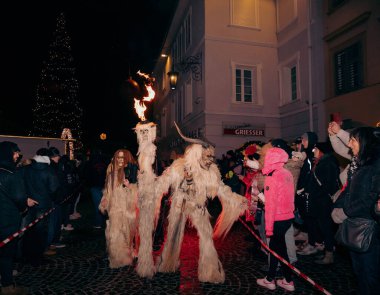 Sankt Veit A D Glan, Avusturya - 4 Ocak 2025: Krampuslauf etkinliği alevler içinde karmaşık kostümler içindeki göstericiler, tatil ışıkları ve dekorasyonları arasında heyecanlı kalabalıklarla meşgul