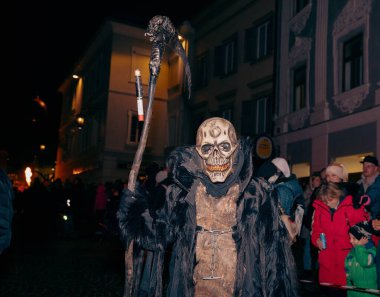 Sankt Veit A D Glan, Avusturya - 4 Ocak 2025: Krampuslauf kutlaması, neşeli bir kalabalık ile, kafatası maskeli ve koyu renk pelerinli bir karakteri sergiliyor