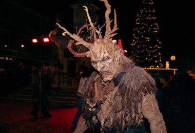 Sankt Veit A D Glan, Avusturya - 4 Ocak 2025: Krampuslauf etkinliği, Krampuslauf 'un detaylı kostüm giymiş korkutucu bir karakterini gösterirken, tatil ışıkları sahneyi aydınlatıyor