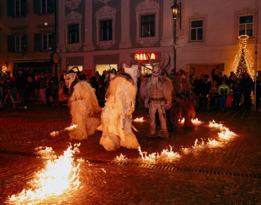 Sankt Veit A D Glan, Avusturya - 4 Ocak 2025: Krampuslauf etkinliği, canlı bir kasaba meydanında ateşin etrafında dans eden özenli kostümlü sanatçılarla birlikte