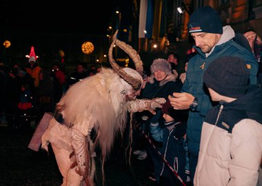 Sankt Veit A D Glan, Avusturya - 4 Ocak 2025: Krampuslauf festivali, canlı bir kış kalabalığı arasında bir çocukla meşgul olan boynuzlu Krampus figürünü yakaladı