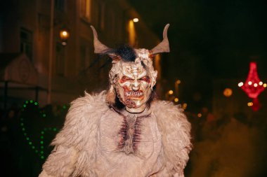 Sankt Veit A D Glan, Avusturya - 4 Ocak 2025: Krampuslauf etkinliği, canlı kalabalık ve şenlikli dekorasyonlar arasında boynuzlu kürk kostümlü korkunç bir şahsiyet sergiliyor