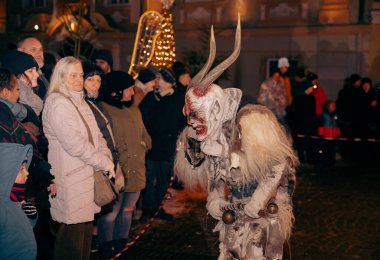Sankt Veit A D Glan, Avusturya - 4 Ocak 2025: Krampuslauf etkinliği, festival dekorasyonları arasında seyirciyle karşılaşan kostüm giymiş boynuzlu bir figürü sergiliyor