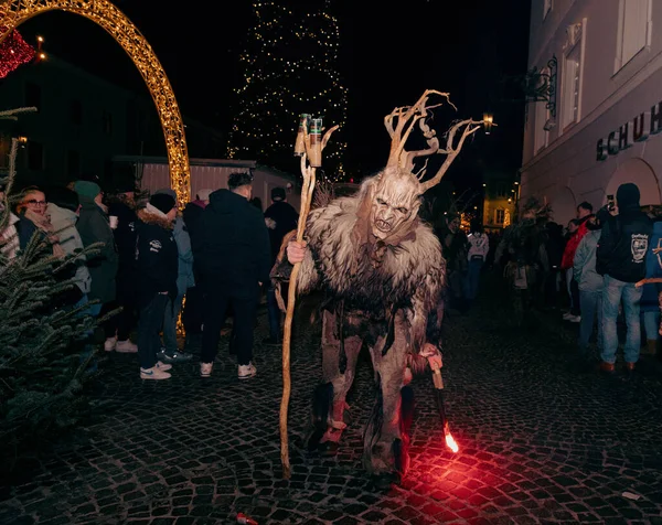 Sankt Veit A D Glan, Avusturya - 4 Ocak 2025: Krampuslauf etkinliği, canlı bir kalabalık ve bayram dekorasyonları arasında boynuzlu ve meşaleli korkunç bir Krampus karakteri sergiliyor