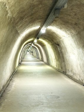 Kıvrımlı tavanları ve beton duvarlarıyla aydınlatılmış yeraltı tüneli..