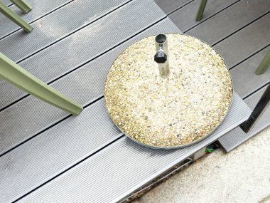 Ahşap balkon güvertesinde yuvarlak taş şemsiye standı.