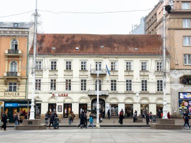 Zagreb, Hırvatistan - 16 Aralık 2025: Kırmızı çatılı ve balkonlu tarihi mimari, yayalar ve dükkanlarla dolu işlek cadde, kentsel yaşamı ve tatil ruhunu yansıtıyor