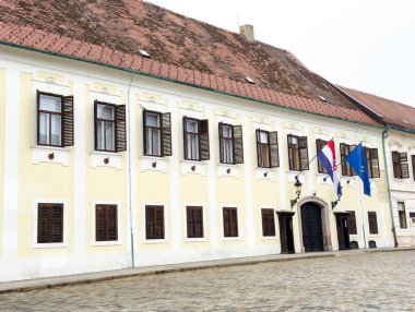 Zagreb, Hırvatistan - 16 Aralık 2025: Kültür mirası ve mimari güzelliği temsil eden ahşap kepenkleri ve kaldırım taşı meydanında bayrakları bulunan tarihi sarı bina