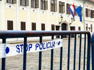 Zagreb, Hırvatistan - 16 Aralık 2025: Emniyet güçleri ve kentsel güvenliği temsil eden tarihi bayraklı, tarihi binanın önündeki dur işareti ile mavi bariyer