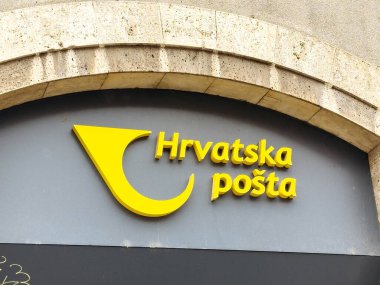 Zagreb, Hırvatistan - 16 Aralık 2025: Hrvatska posta tabelasında, kopya alanı olan kentsel bir çevrede posta hizmetlerini temsil eden taştan bir duvarda parlak sarı bir logo görülüyor