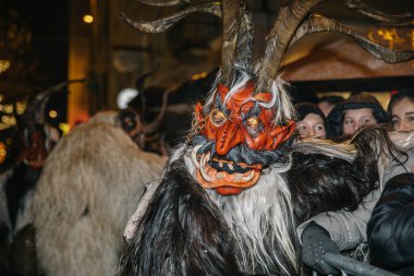 Villach, Avusturya - 01 Aralık 2023: Krampus geleneksel figürü Krampuslauf festivalinde karmaşık maskeli ve boynuzlu, neşeli kalabalık ve tatil ruhu ile çevrili