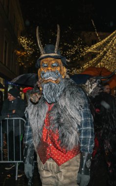 Villach, Avusturya - 01 Aralık 2023: Krampuslauf festivaline katılan, Krampus kostümlü, şenlikli atmosfer ve tatil dekorasyonlarıyla çevrili