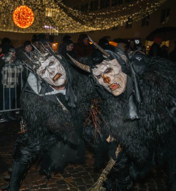 Villach, Avusturya - 01 Aralık 2023: Krampus kostümlü iki kişi, Krampuslauf kutlamalarının ruhunu somutlaştıran festival ışıkları altında bir arada duruyorlar