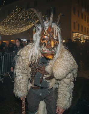 Villach, Avusturya - 01 Aralık 2023: Krampus gibi giyinmiş boynuzlu bir adam, canlı bir bayram kutlamasının ortasında Krampuslauf 'a katılıyor.