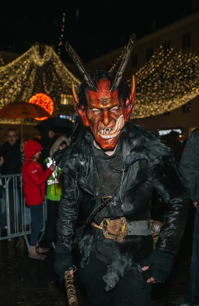Villach, Avusturya - 01 Aralık 2023: Krampus gibi giyinmiş adam, neşeli ışıklar ve canlı kalabalığın arasında canlı maske ve koyu renk giysiler sergiliyor.