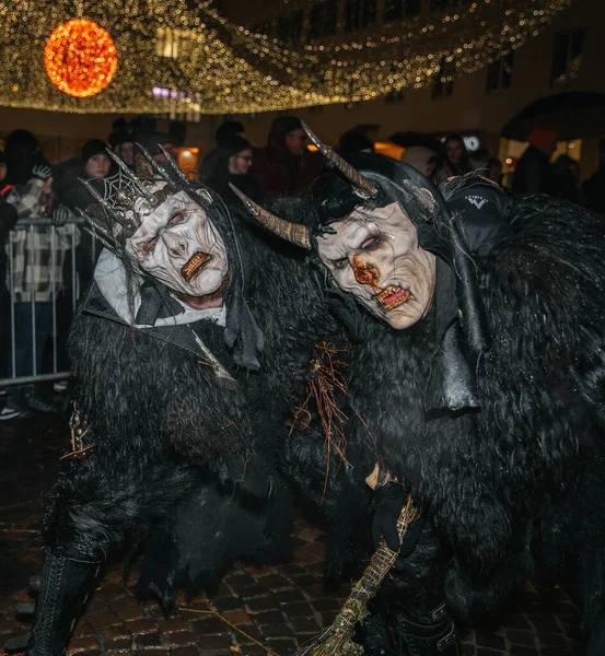 Villach, Avusturya - 01 Aralık 2023: Krampus kostümlü iki kişi, Krampuslauf kutlamalarının ruhunu somutlaştıran festival ışıkları altında bir arada duruyorlar